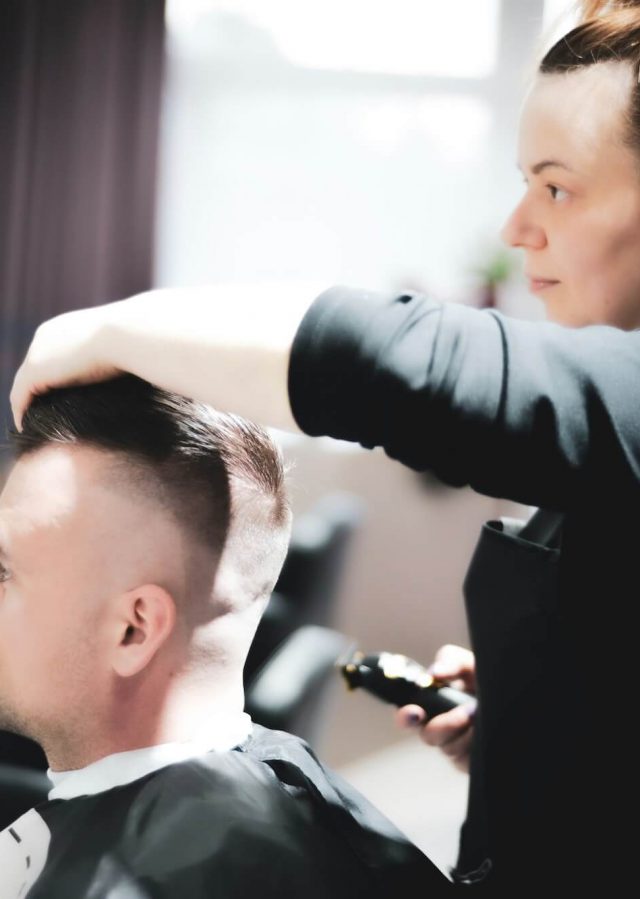 Young stylist trimming and styling a man's hair